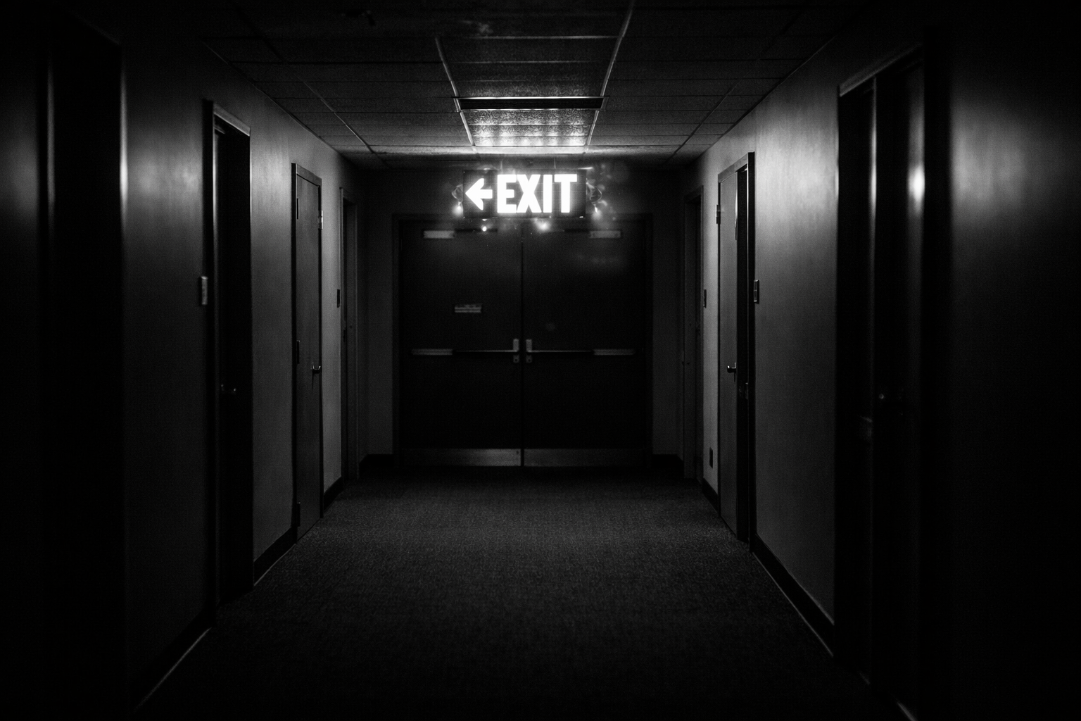 Dim hallway with bright exit sign and closed door at end