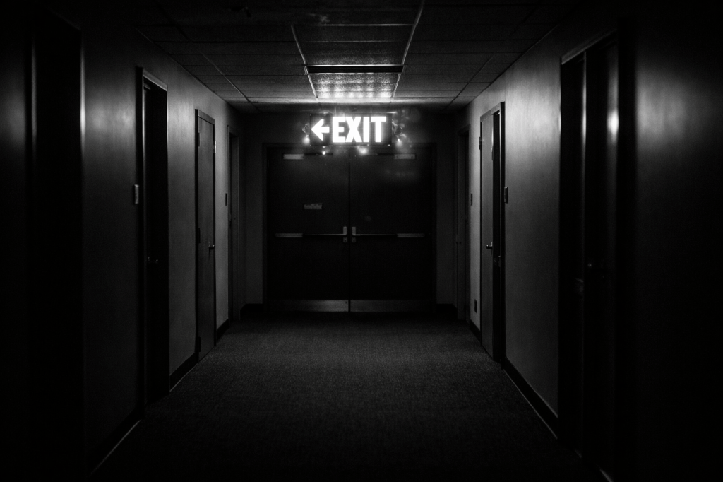 Dim hallway with bright exit sign and closed door at end