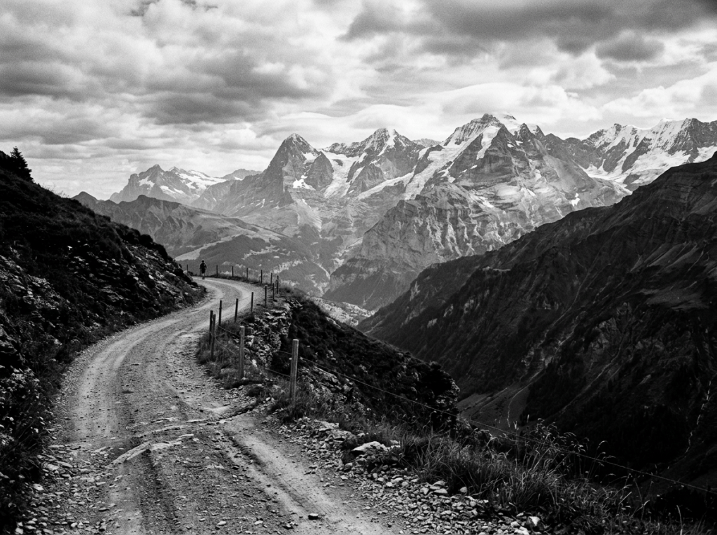 Rugged alpine trail overlooking snow-capped mountain peaks beneath cloudy skies
